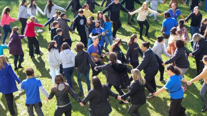 pessoas de mãos dadas em um jardim, com dois homens ao centro tocando violão.